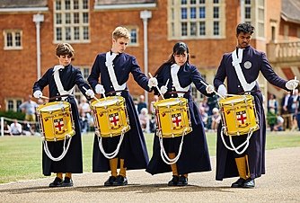 Students in uniform drumming during a school parade performance.
