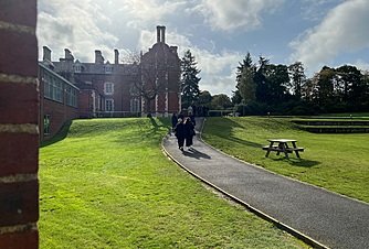 A sunny day in which a group of ladies is walking along a path towards a large school building