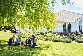 students in their uniforms are sitting underneath a tree on the grass chatting