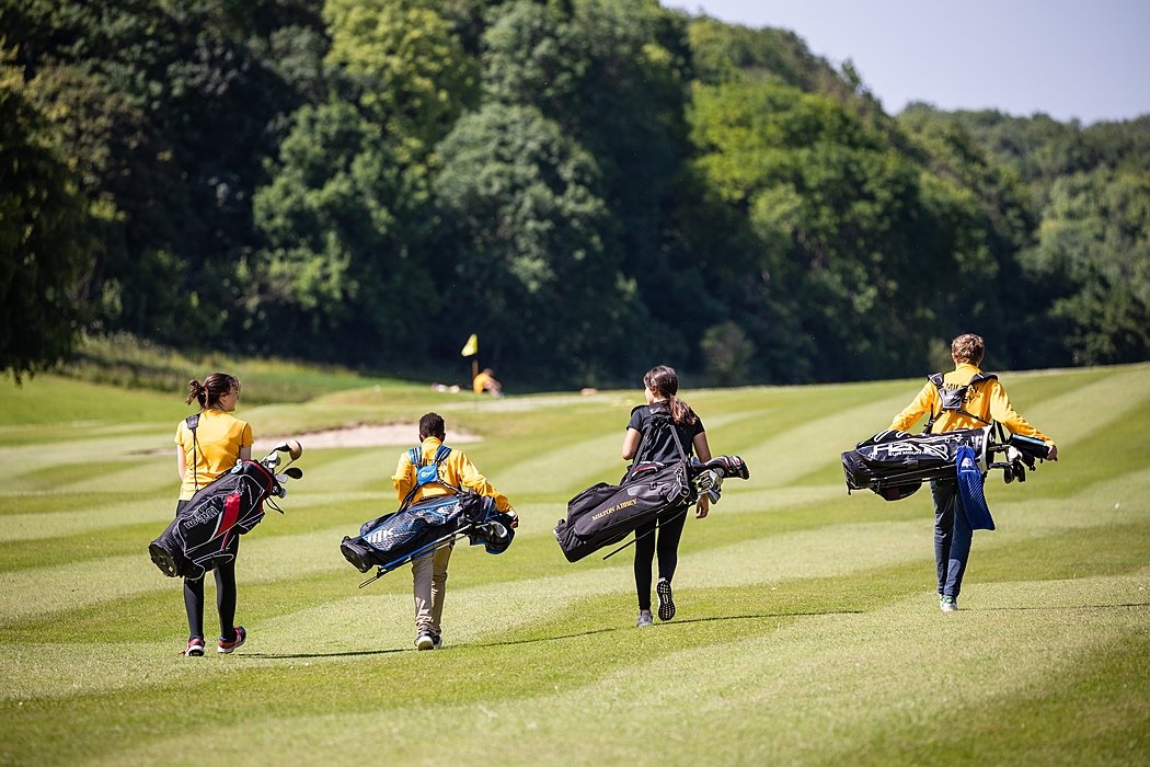 four golf players on the golf course from behind carrying their heavy golf bags