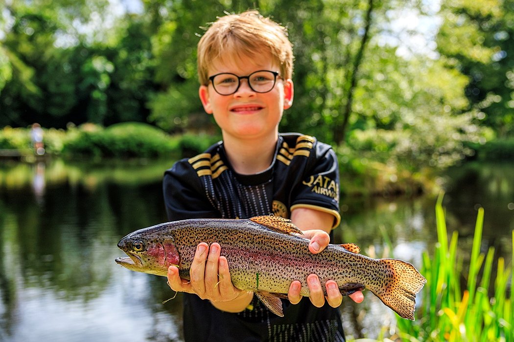 A boy with glasses holding proudly a trout into the camera during Sedbergh International Summer School