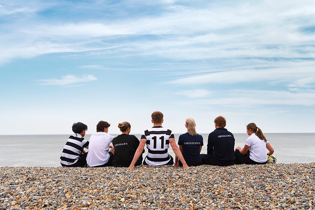Gresham's School pupils sitting on a pebbly Norfolk beach