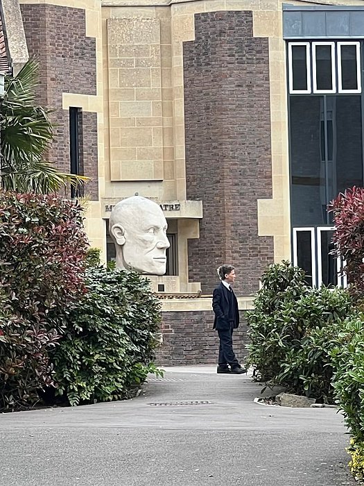theatre with the buste of a big head, a boy infront of it in a school uniform
