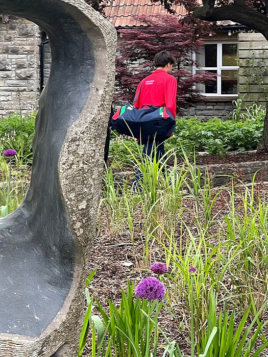 Students with a sports bag over his shoulder walking over the green school campus