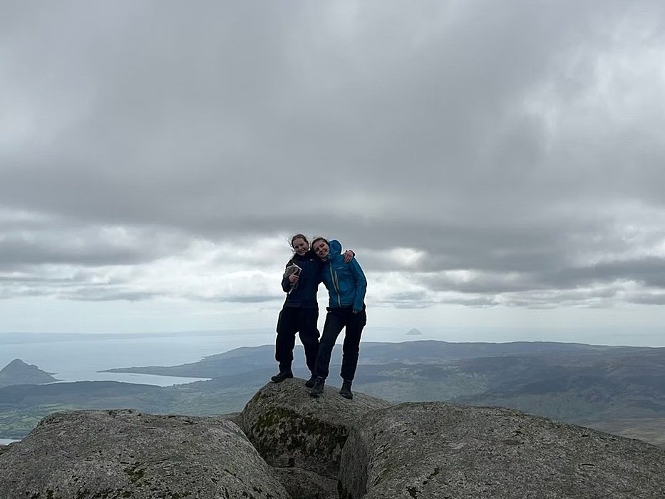Two girls in hiking gear on top of a mountain in grey weather