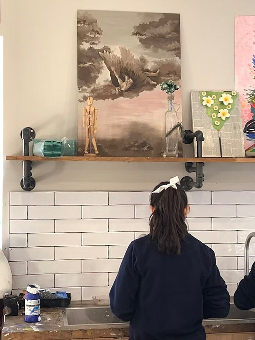 Girl infront of a sink, art on a shelf on top of her