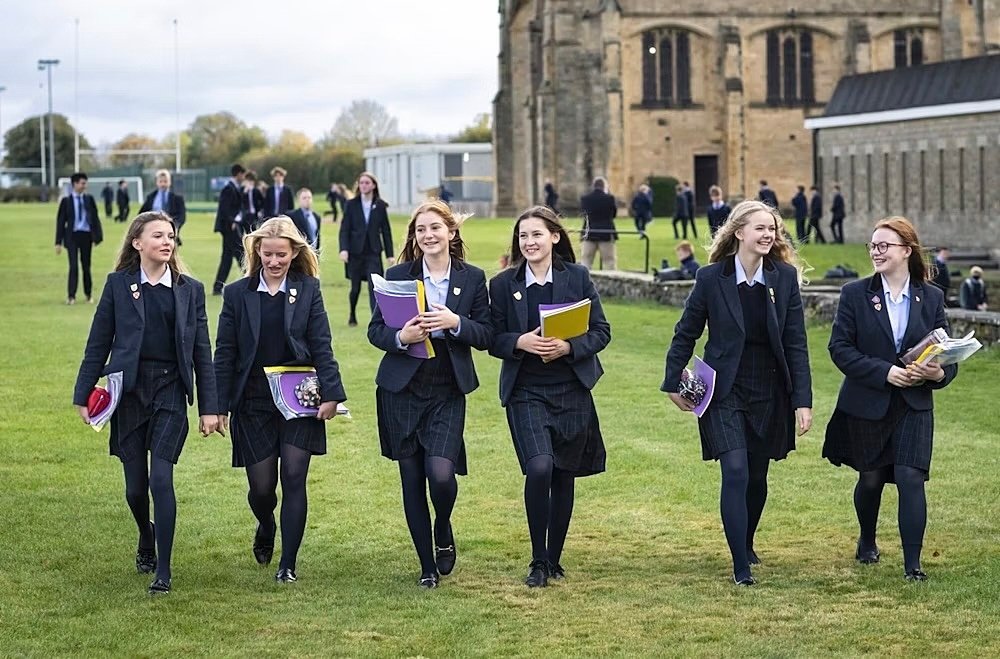 Group of students in uniforms walking together on the school grounds, smiling and chatting.