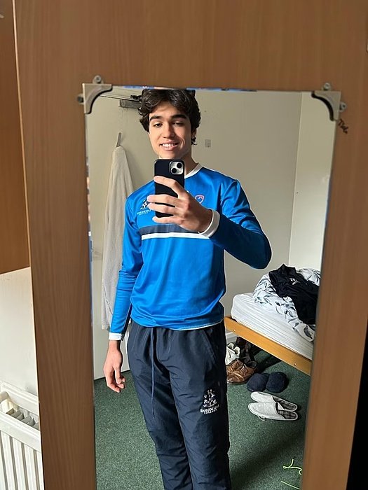 A student takes a mirror selfie in a dorm room while wearing blue sports clothes.