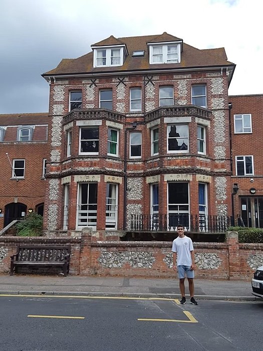 A person stands on the pavement in front of a large red-brick building with white-framed windows.