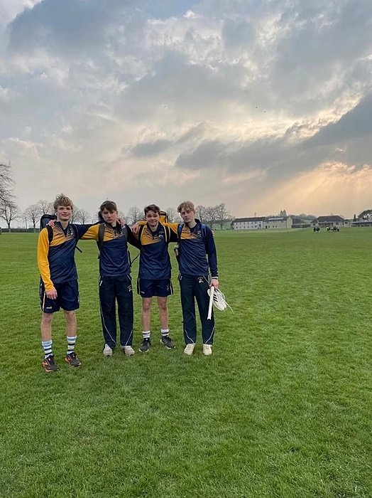 Four students in matching sportswear standing together on a large grass field under a cloudy sky.