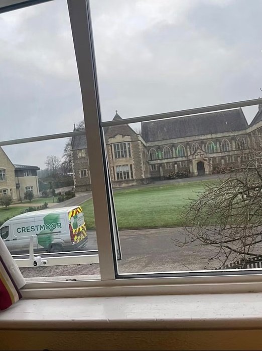View through a window showing a historic school building and a parked van on the grounds.