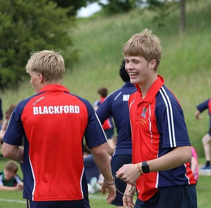 Students in red and blue sports uniforms laughing and talking during outdoor sports practice.