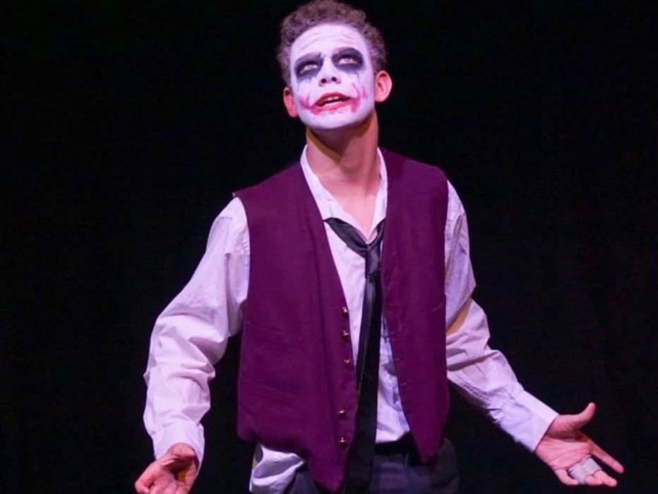 A young actor wearing face paint resembling the Joker character performing on stage.