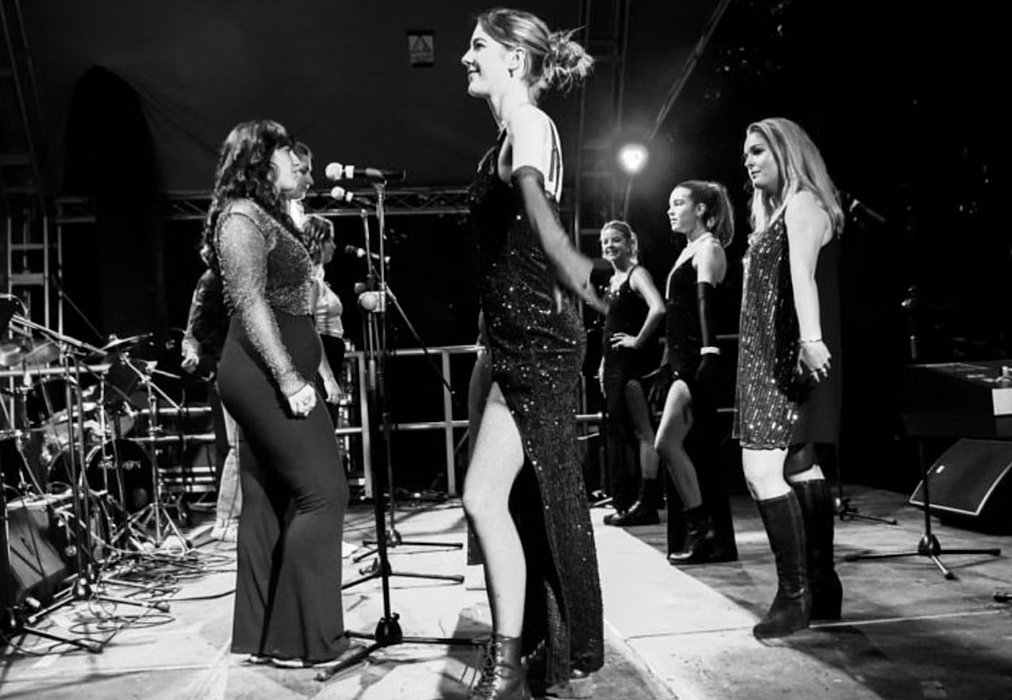 A group of women performing on stage in elegant black outfits during a musical show.