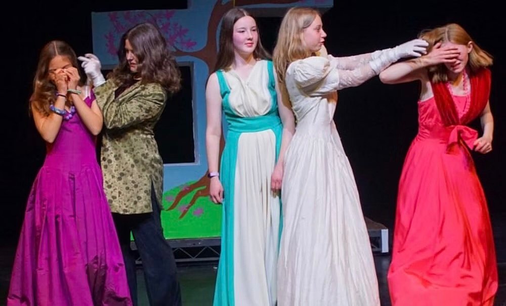 Five students acting on stage in colorful costumes during a theatre play.