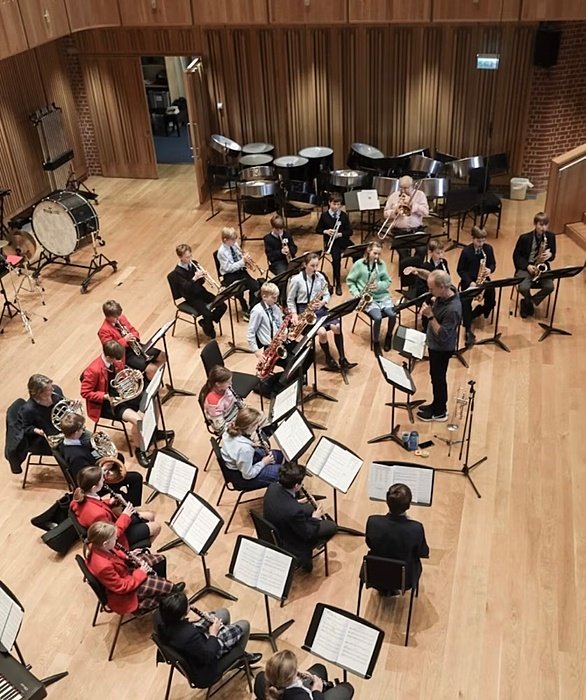 A group of students playing musical instruments in an orchestra rehearsal with a conductor.