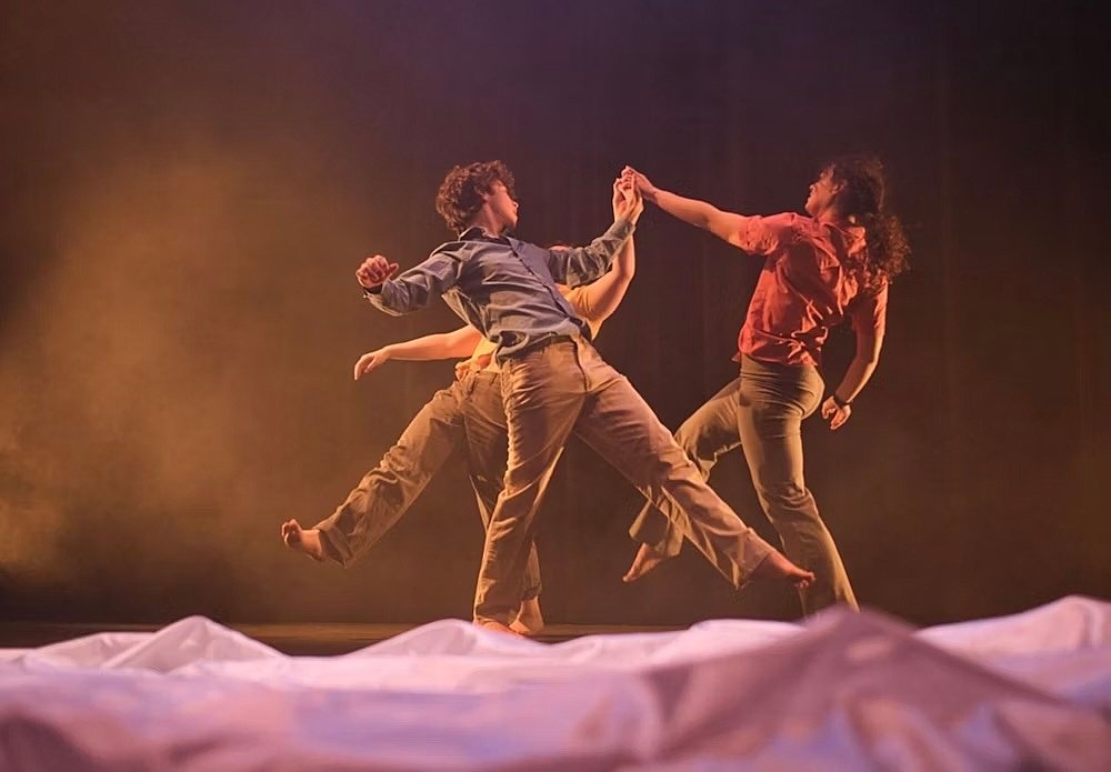 Three dancers performing a contemporary dance on stage under warm lighting.