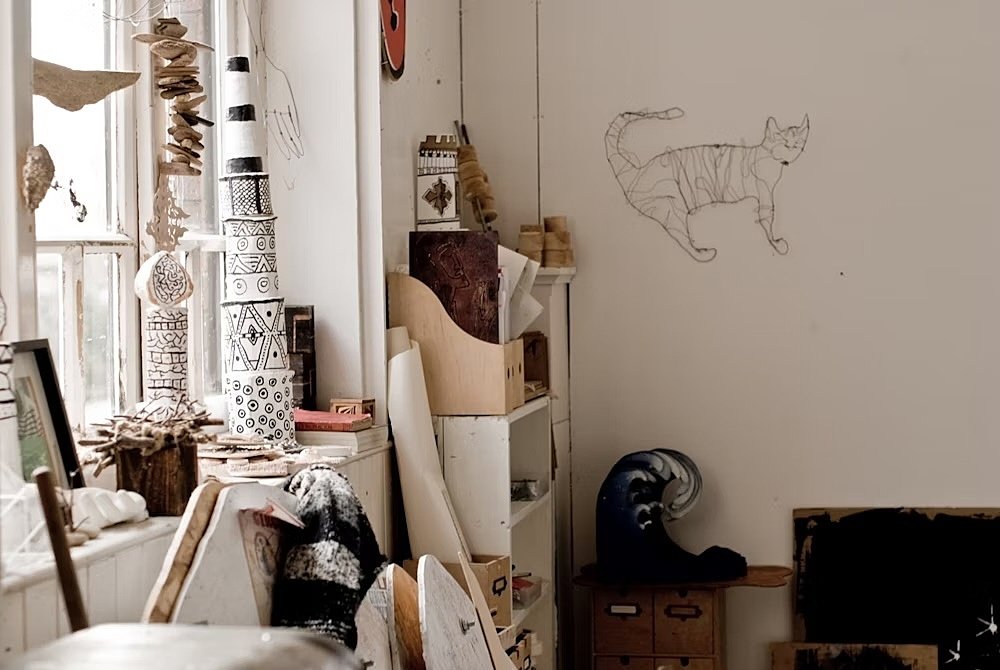 A well-lit room with art exhibits, including a wire cat on the wall