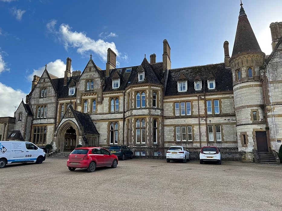 Historic stone building with gothic-style architecture and parked cars in front.
