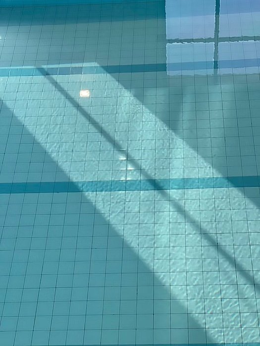 Close-up of swimming pool tiles with sunlight reflecting on the water.