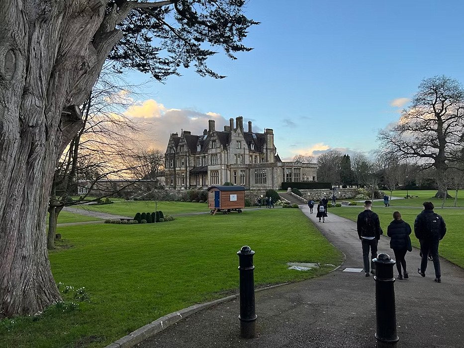 Students walking along a path toward a grand historic school building surrounded by gardens.
