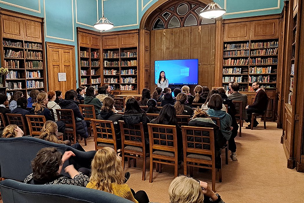 A group of girls sitting in a library, listening to a teacher giving a talk
