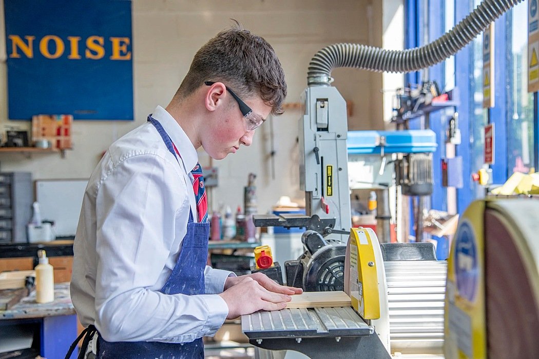A boy with safety-goggles on working on a wood-saw