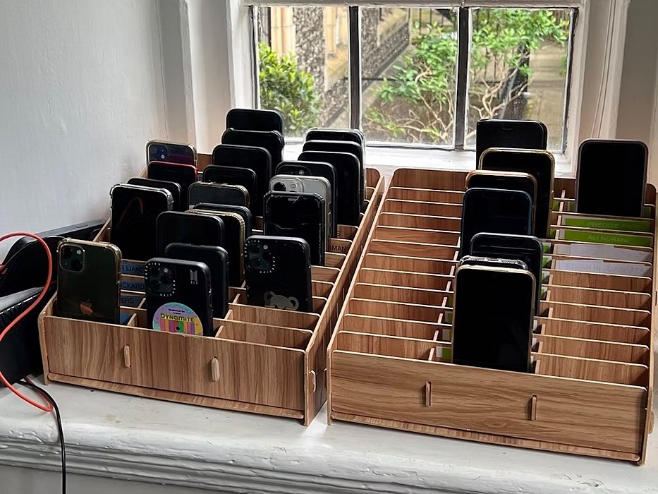 a wooden storage box with slots full of smartphones for during the day