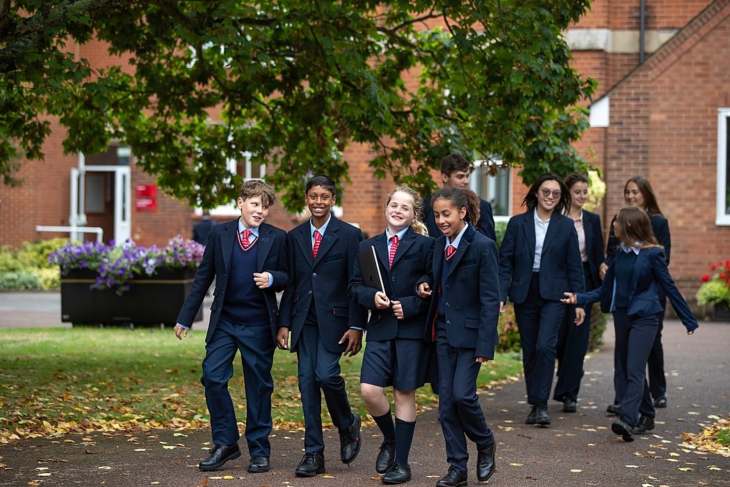 Group of students in school uniforms walking and chatting happily under trees on campus.