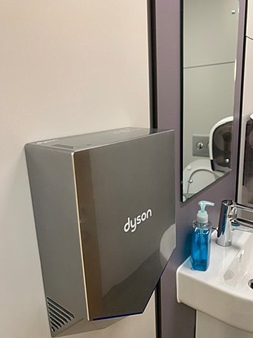Silver Dyson hand dryer mounted on a clean white restroom wall