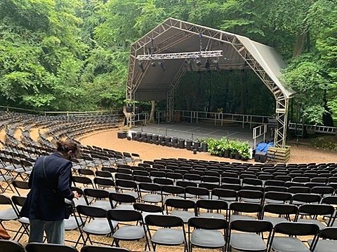 Outdoor stage with rows of chairs surrounded by tall trees