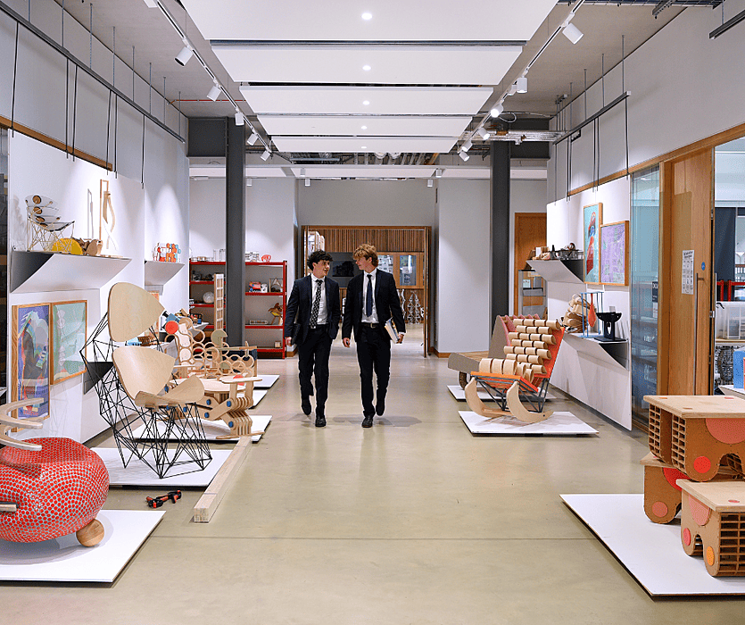 Two students walking through a design studio displaying creative furniture and artwork.