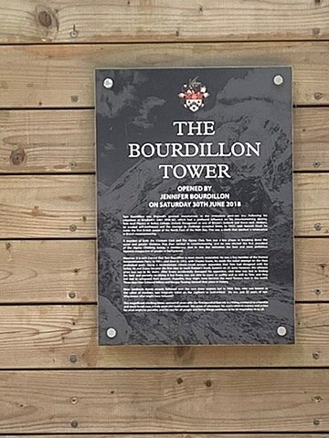 Memorial plaque mounted on wooden wall near outdoor tower