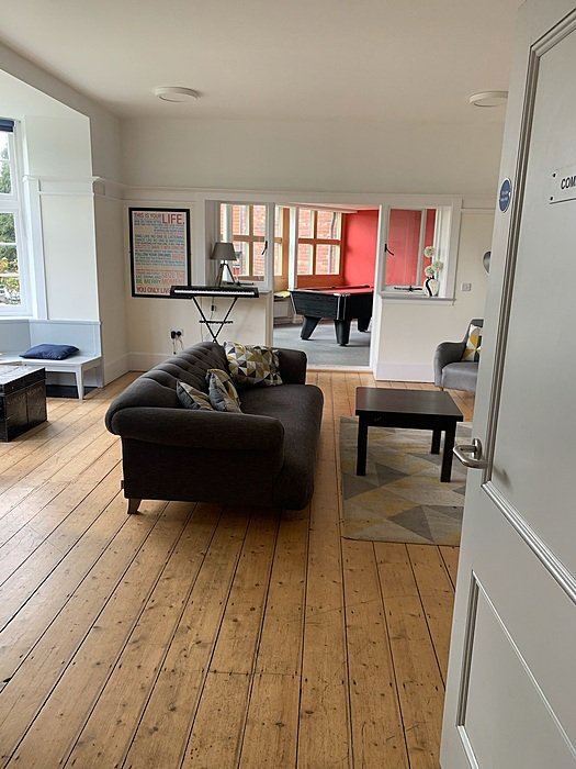 A bright communal room with a grey sofa, wooden flooring and a pool table in the adjoining room.