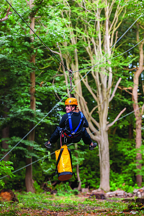 A female student in a climbing harness on a rope in the school's woodland high rope course