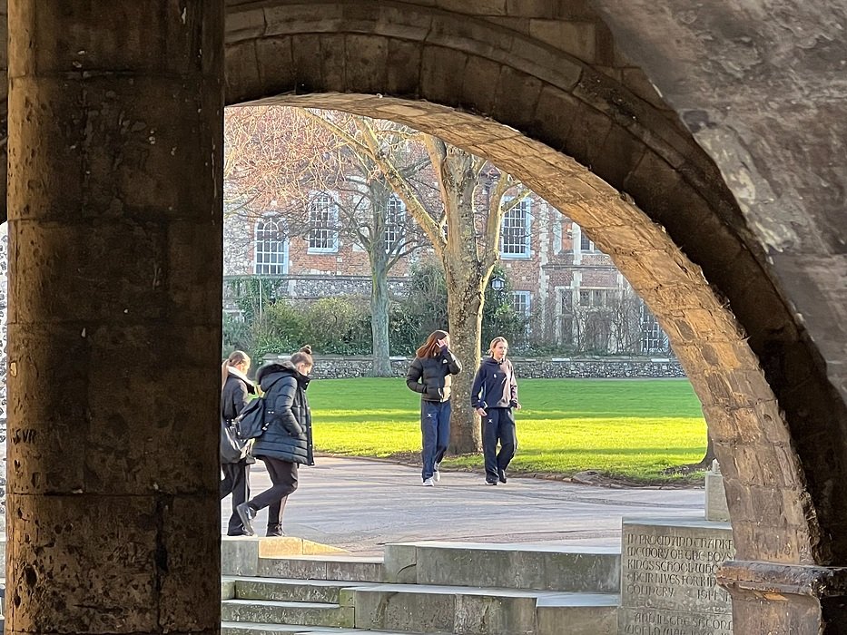 Students walking through stone archway on a sunny school campus.