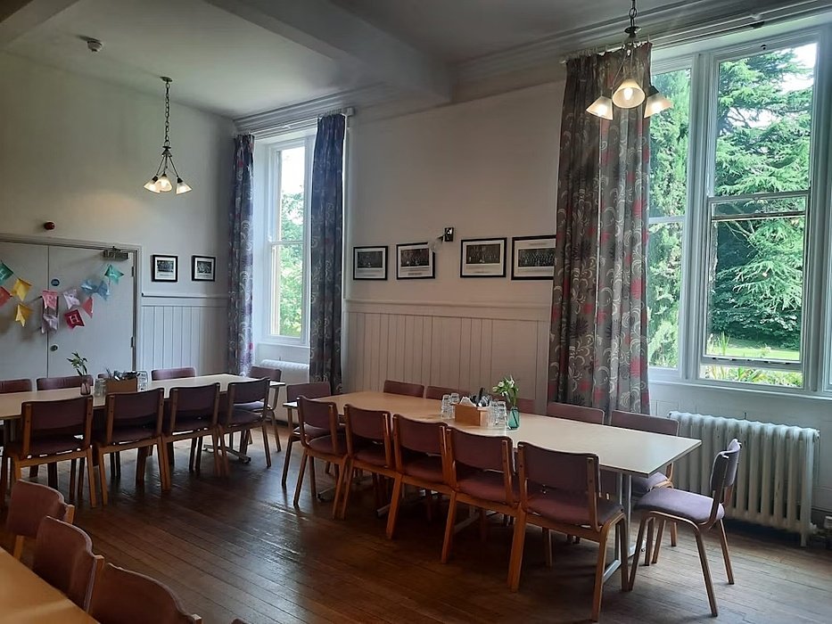 A dinding hall with big windows and long wooden tables and chairs
