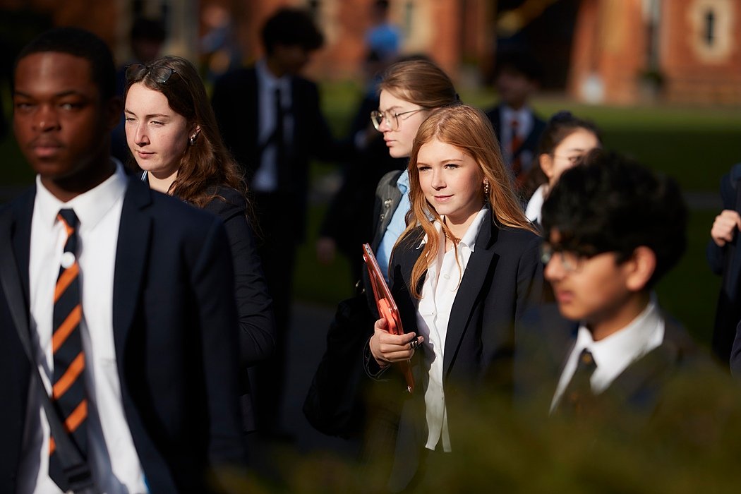 Students in formal school uniforms walking together outdoors on a sunny day.