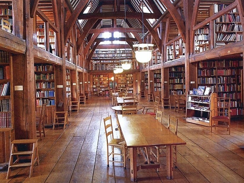 Wooden library, shelves on both sides on two floor, open plan, tables and chairs in the middle