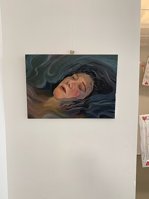 A painting shows a woman’s face with closed eyes, surrounded by dark, flowing lines.