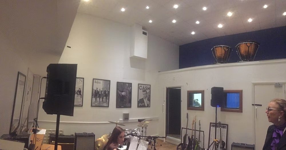 A music room with instruments, speakers, and framed posters on the wall.