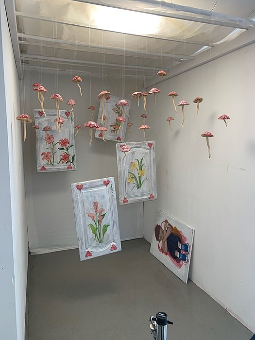 Pink and red paper flowers hang from the ceiling of a white room, with floral drawings displayed on the walls.