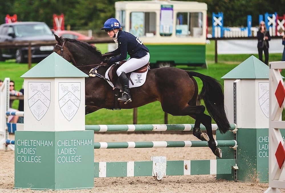 A girls jumps with a horse over a hurdle that reads Cheltenham Ladies College