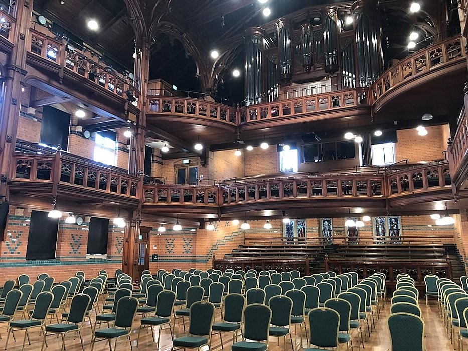 Grand hall featuring two galleries, an organ, and rows of chairs on the parquet