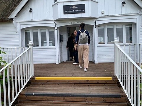 People entering a white wooden art building with stairs