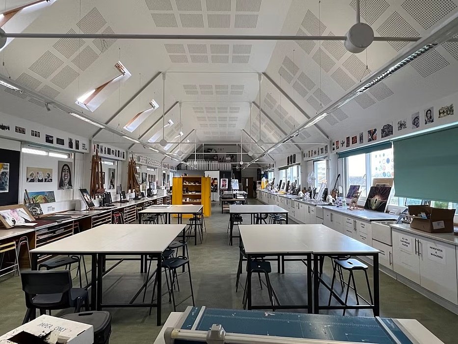 Spacious art classroom with high ceiling, tables, easels, and student artwork displayed along the walls.
