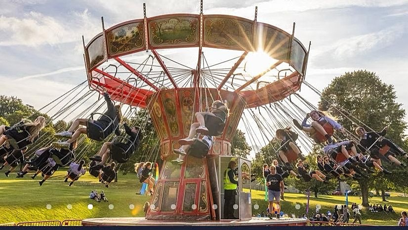 People enjoy a vintage swing ride in a park as the sun shines through the carousel’s structure.