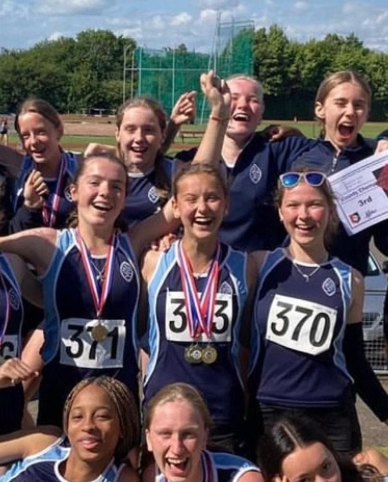 A group of smiling school athletes wearing navy blue uniforms celebrate together, some holding medals.