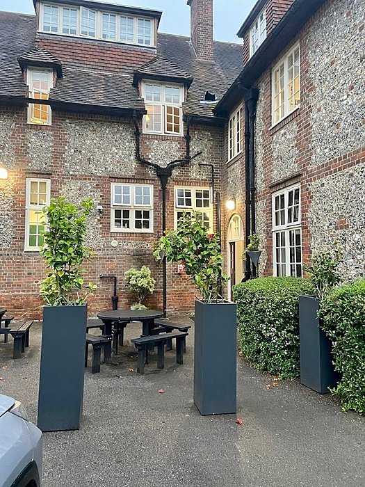 A courtyard area of a brick building with tall planters, benches, and a round table.