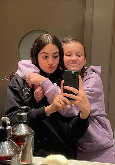 Two friends in hoodies take a mirror selfie together, smiling and posing playfully.